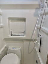 Inside an RV rental: a compact white wet bath featuring a toilet, shower hose, and a practical storage shelf.