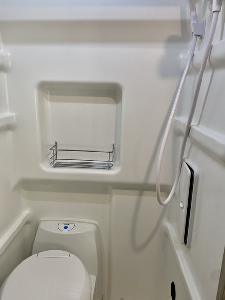 Inside an RV rental: a compact white wet bath featuring a toilet, shower hose, and a practical storage shelf.