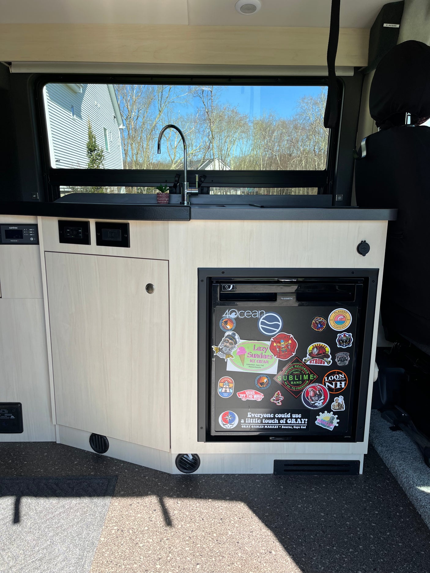 View of an RV rental's cozy kitchen: light wood cabinets, sink, and a sticker-covered Dometic fridge.