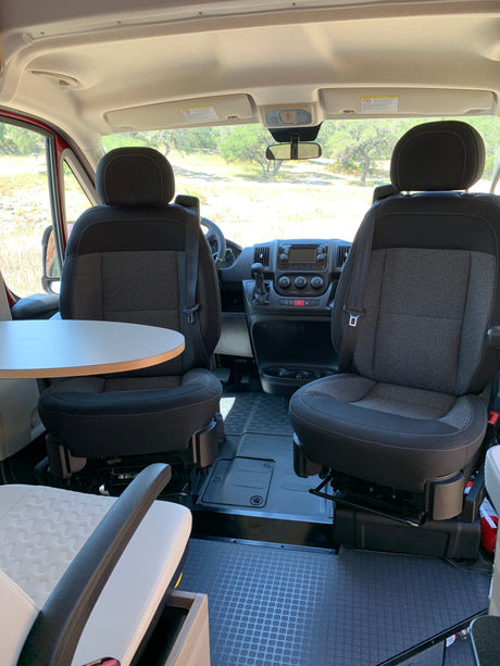 Spacious RV rental interior: front cockpit view with swivel seats, dashboard, and a convenient table. Perfect for road trips.