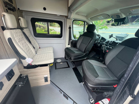 Spacious RV rental interior, showcasing comfortable quilted seating, driver's cabin, and textured floor.