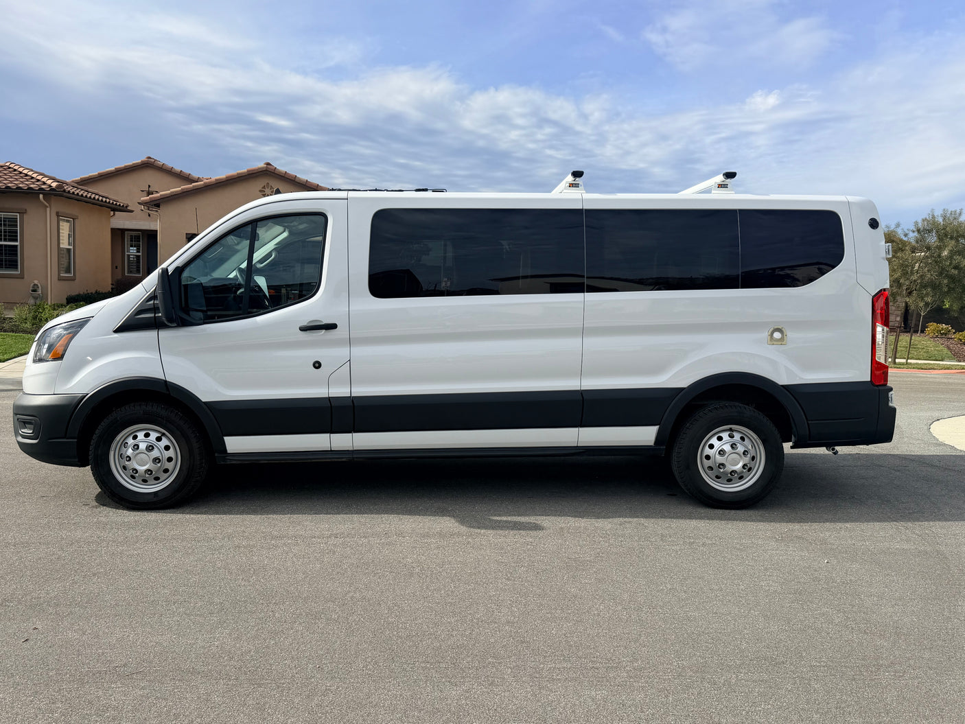 A pristine white van with dark tinted windows and rooftop vents/racks, possibly an RV rental, parked on a residential street.