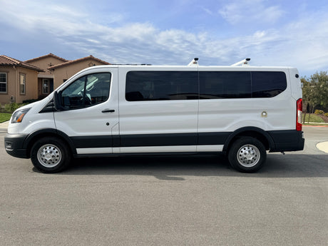 A pristine white van with dark tinted windows and rooftop vents/racks, possibly an RV rental, parked on a residential street.