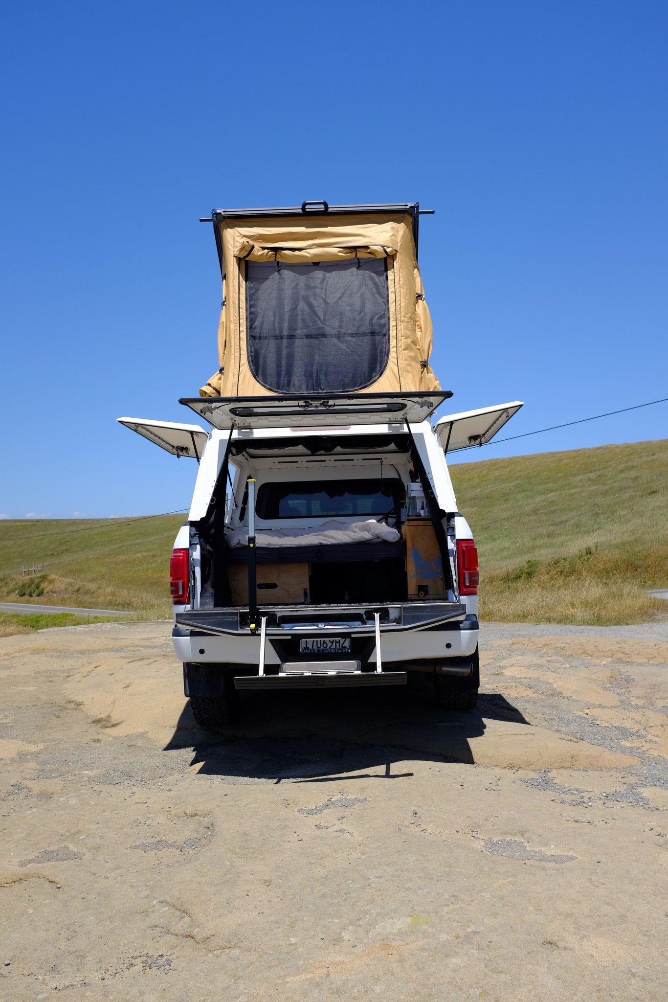 rv rental: White pickup truck with deployed rooftop tent, open camper shell revealing a sleeping setup. Ready for outdoor adventure! — photo 4