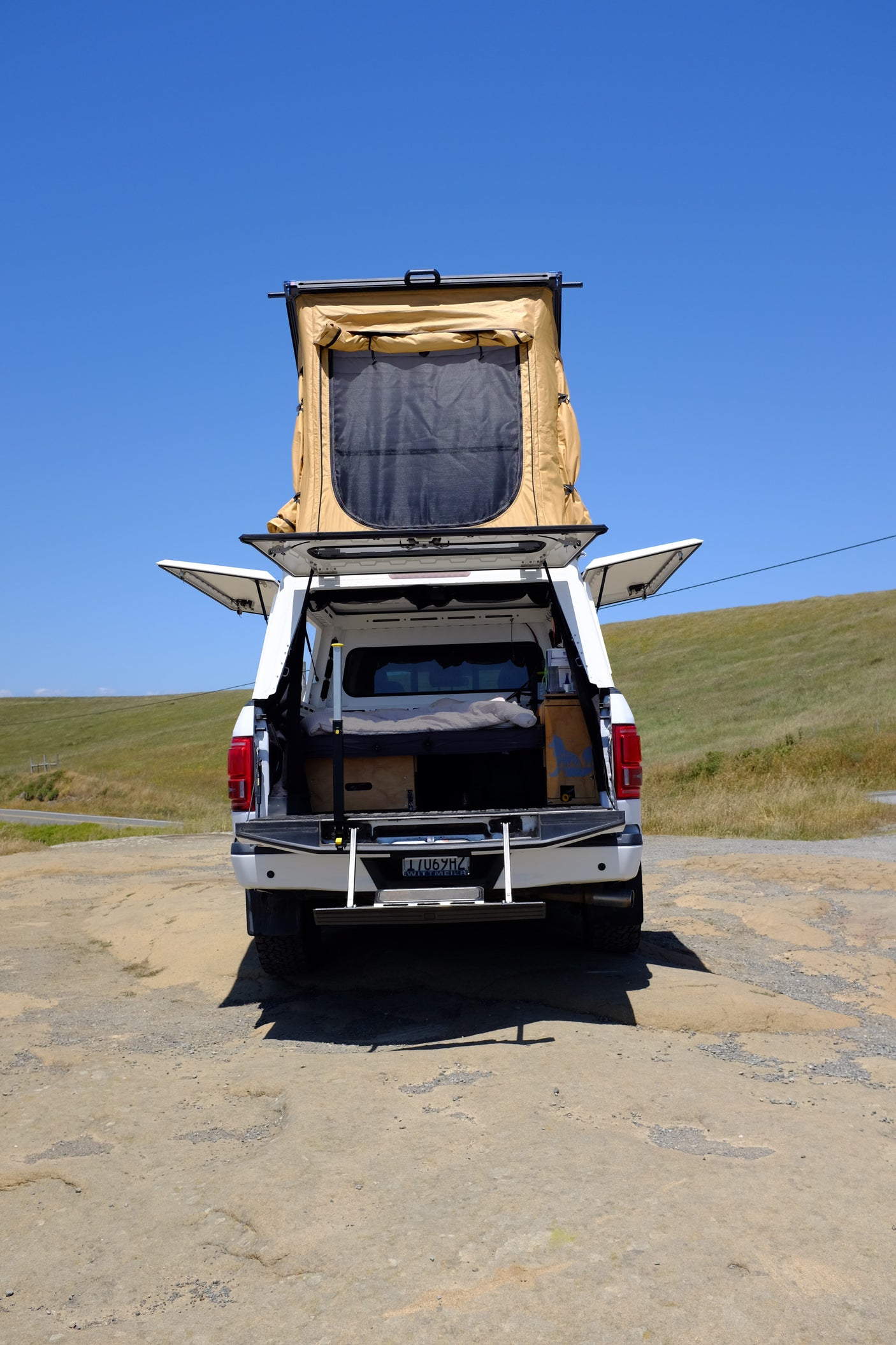 rv rental: White pickup truck with deployed rooftop tent, open camper shell revealing a sleeping setup. Ready for outdoor adventure!