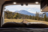 Wake up to stunning mountain views from your cozy RV rental bed, surrounded by forests and a dirt road leading to adventure.