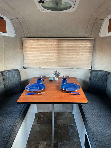 Cozy RV rental dinette area featuring a set table for two with blue plates, mugs, and decor. Ideal for travel.