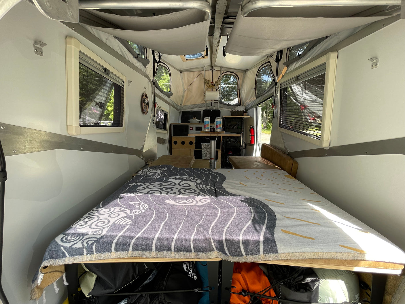 Cozy rv rental interior: A pop-up camper features a large bed in the foreground, with a compact kitchen area further back.