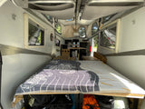 Cozy rv rental interior: A pop-up camper features a large bed in the foreground, with a compact kitchen area further back.