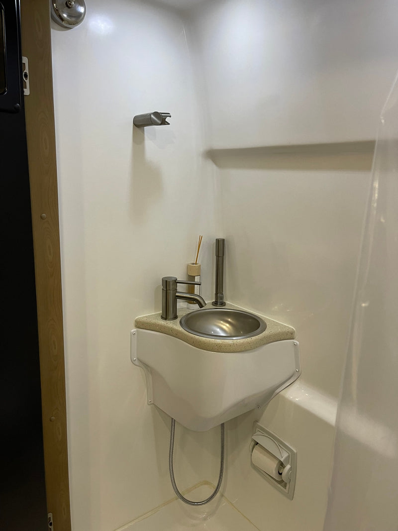 RV rental compact wet bath featuring a corner sink, shower holder, and toilet paper dispenser. — photo 14