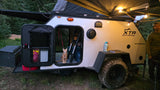 This off-road RV rental features a teardrop camper with an awning, string lights, and a cat, ideal for camping adventures.