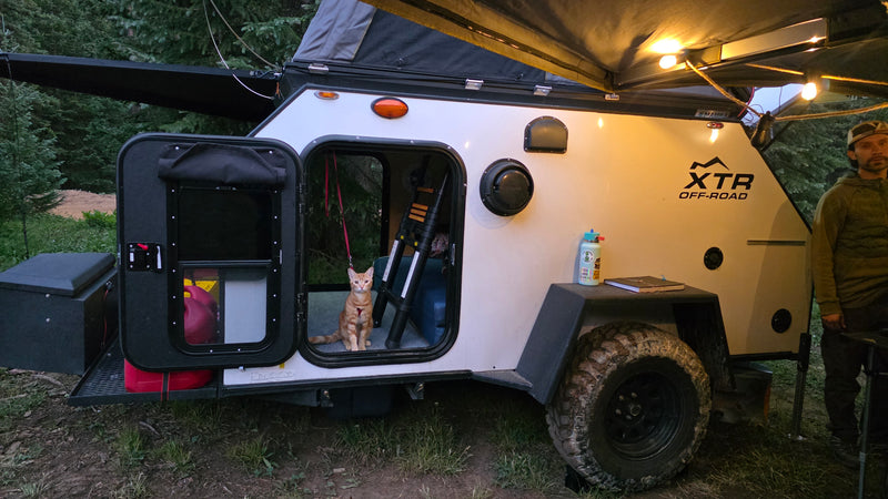 This off-road RV rental features a teardrop camper with an awning, string lights, and a cat, ideal for camping adventures. — photo 6