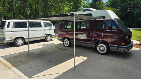 Maroon VW Westfalia camper van with extended awning beside a white VW Vanagon, ready for RV rental adventures.