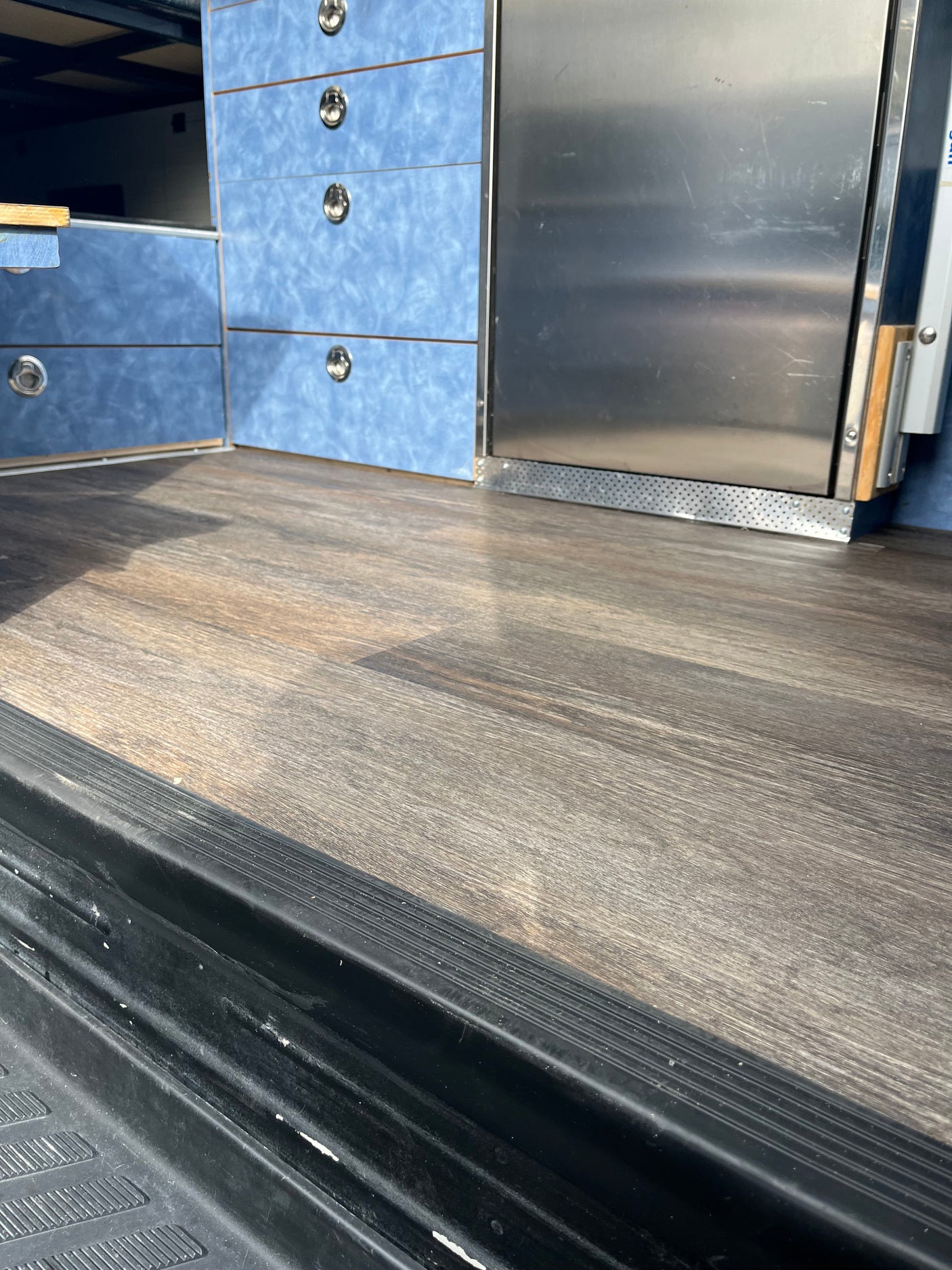 Inside an rv rental: wood-look floor, blue storage drawers with silver handles, and a stainless steel fridge.