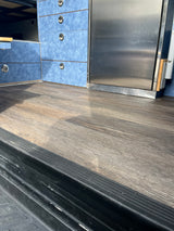 Inside an rv rental: wood-look floor, blue storage drawers with silver handles, and a stainless steel fridge.