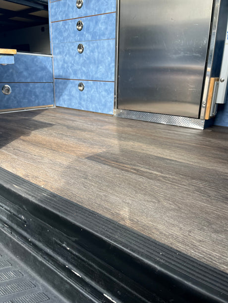 Inside an rv rental: wood-look floor, blue storage drawers with silver handles, and a stainless steel fridge.