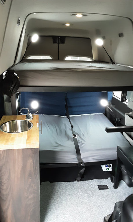 RV rental interior: cozy camper van with bunk beds, sink, and built-in amenities for travel.
