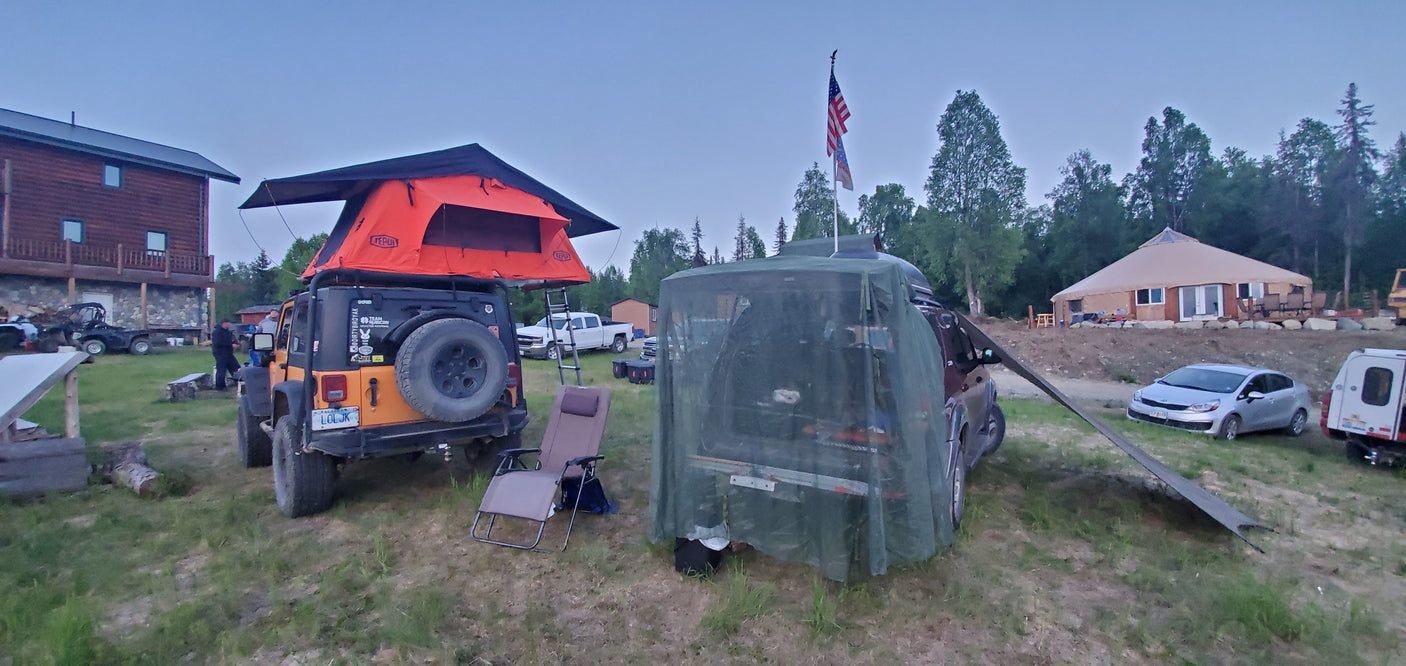 RV rental vacation setup: Jeep with rooftop tent & netted SUV at a camp with a lodge and yurt.