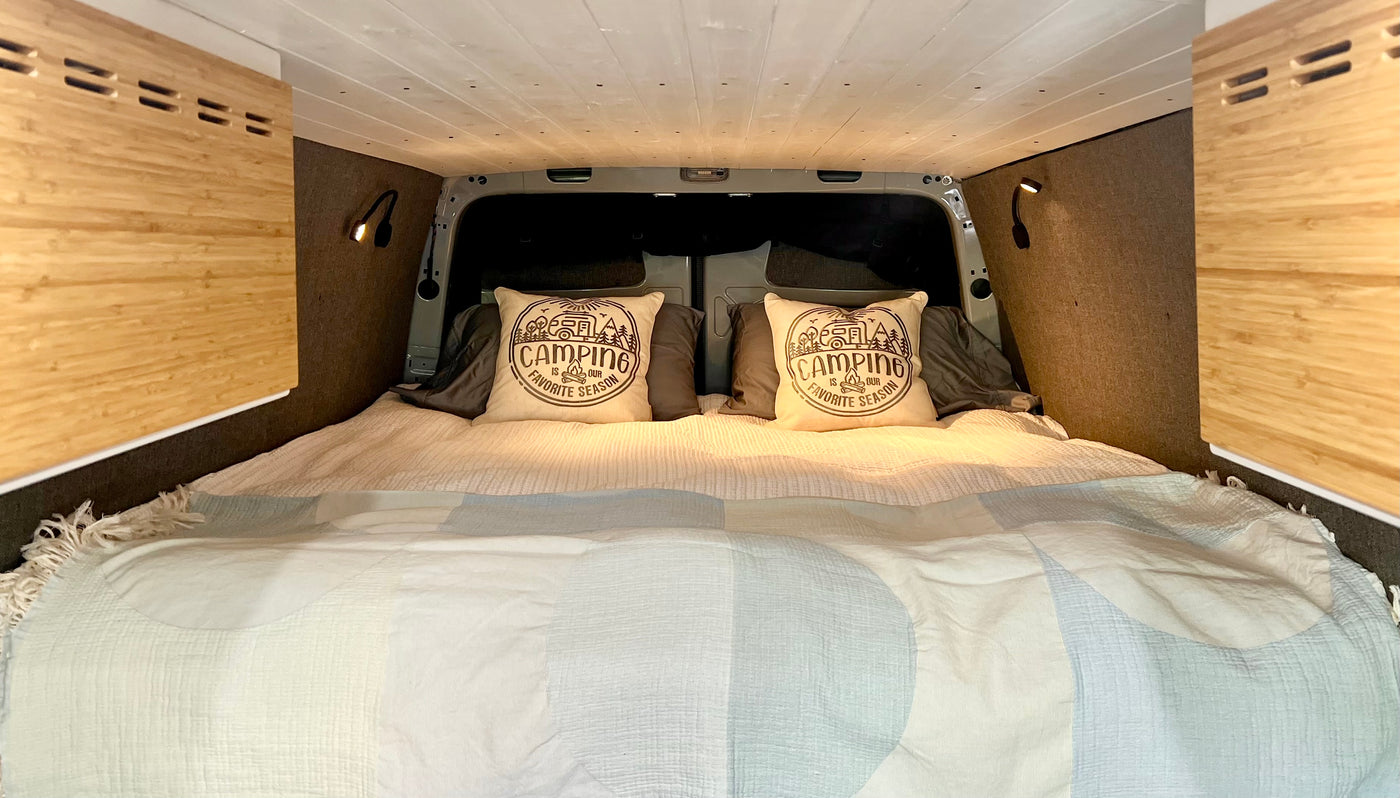 Inviting camper van bed, ready for your RV rental adventure. Soft bedding, custom wood panels, and fun camping pillows. — photo 5