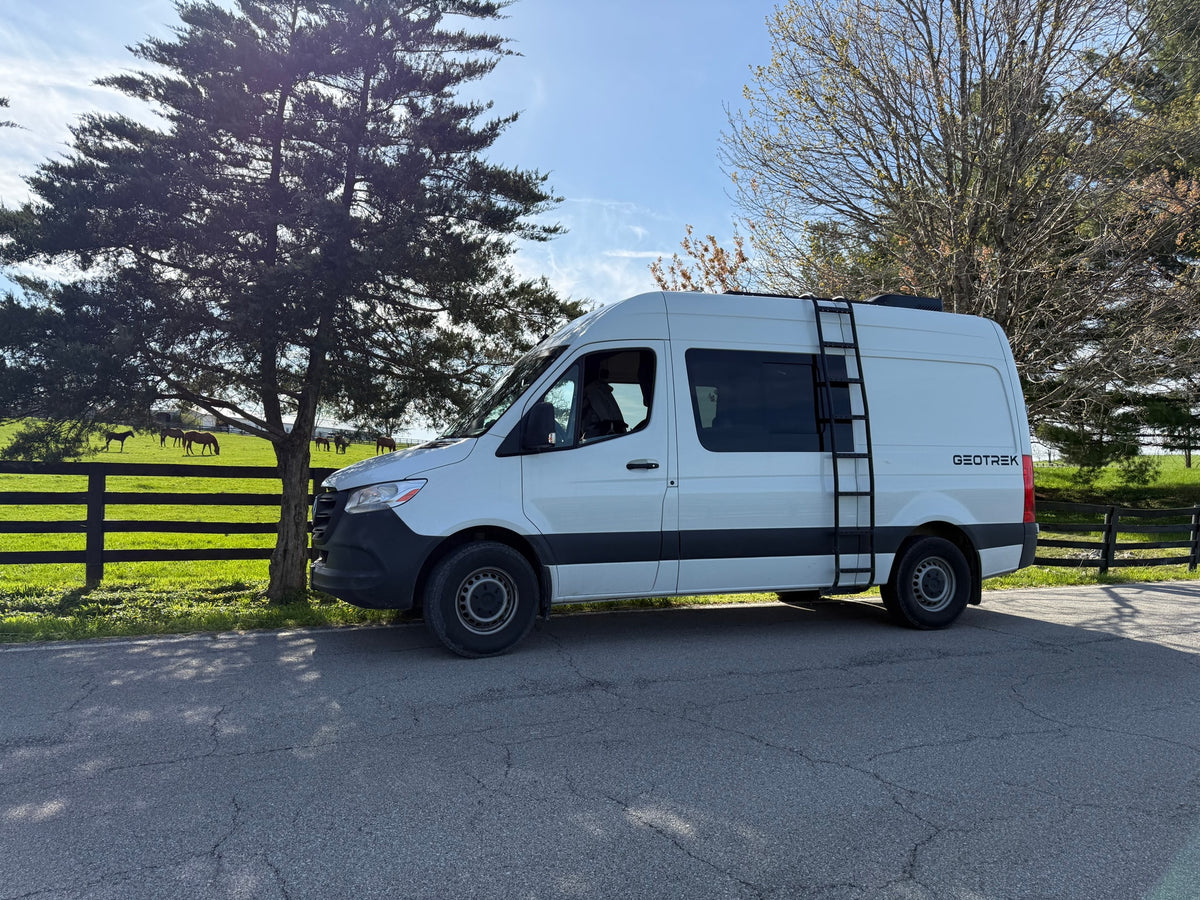 Experience nature with this Geotrek rv rental! White adventure van parked by a serene horse farm & green fields.