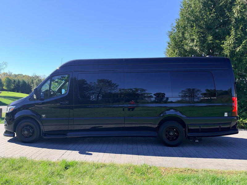 likely an RV rental. Parked on a drive with trees & blue sky.|Sleek black Mercedes-Benz Sprinter conversion van with "ULTIMATE TOYS" badge — photo 2