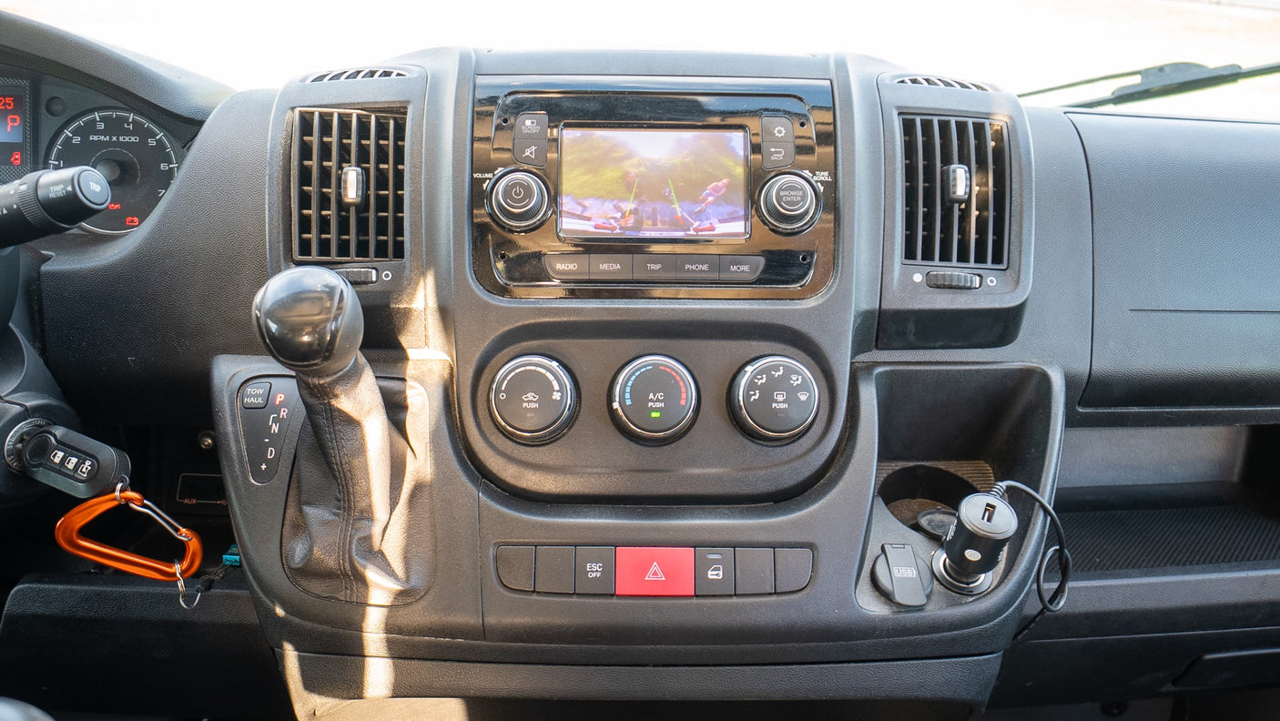 Inside an RV rental van: Dashboard view with infotainment screen, climate controls, and gear shifter, ready for the road.