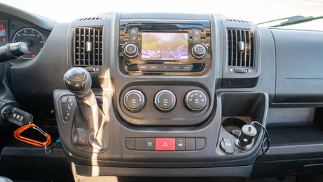 Inside an RV rental van: Dashboard view with infotainment screen, climate controls, and gear shifter, ready for the road.