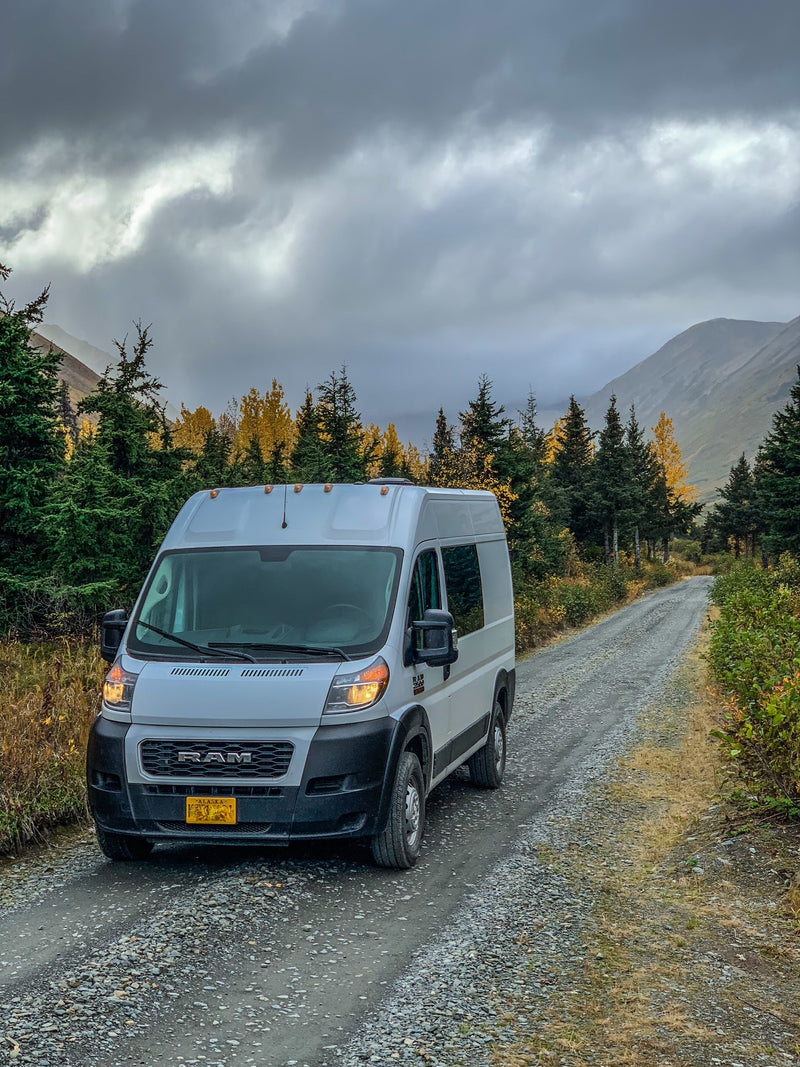 White RV rental van on a gravel road in the Alaskan mountains, surrounded by vibrant autumn trees under a cloudy sky. — photo 9