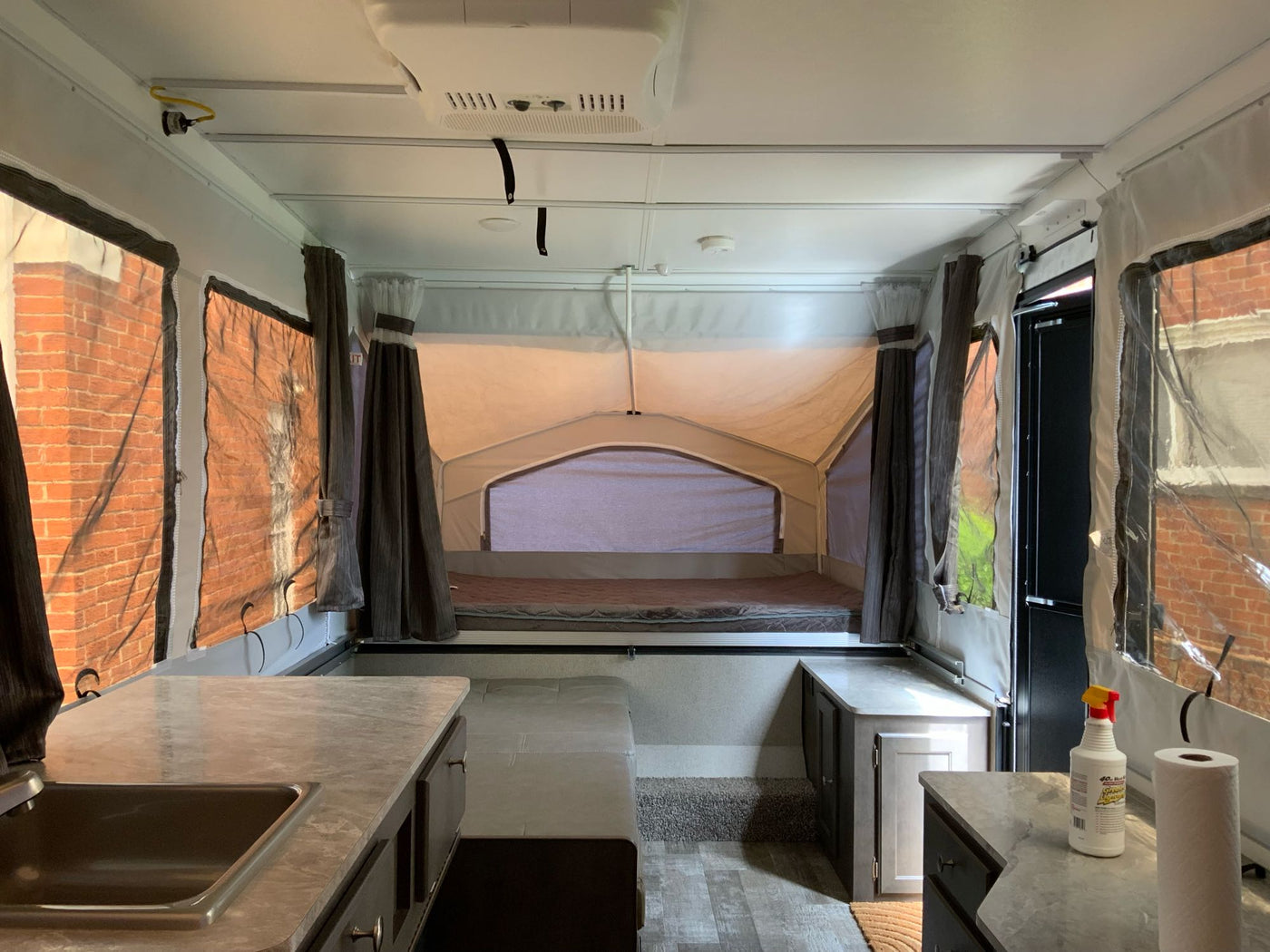  tall trees silhouetted against the sky.|Inside a bright RV rental pop-up camper with comfortable beds