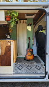 Cozy RV rental interior with a kitchenette, plants, guitar, and modern decor, perfect for mobile adventures.