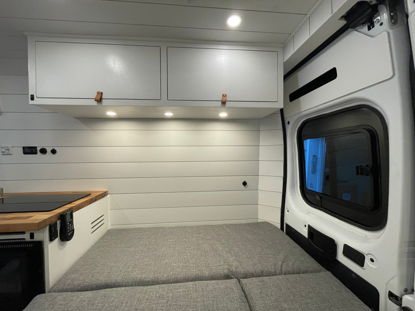 Modern RV rental interior with shiplap walls, overhead cabinets, a small kitchen, and comfy gray bed.