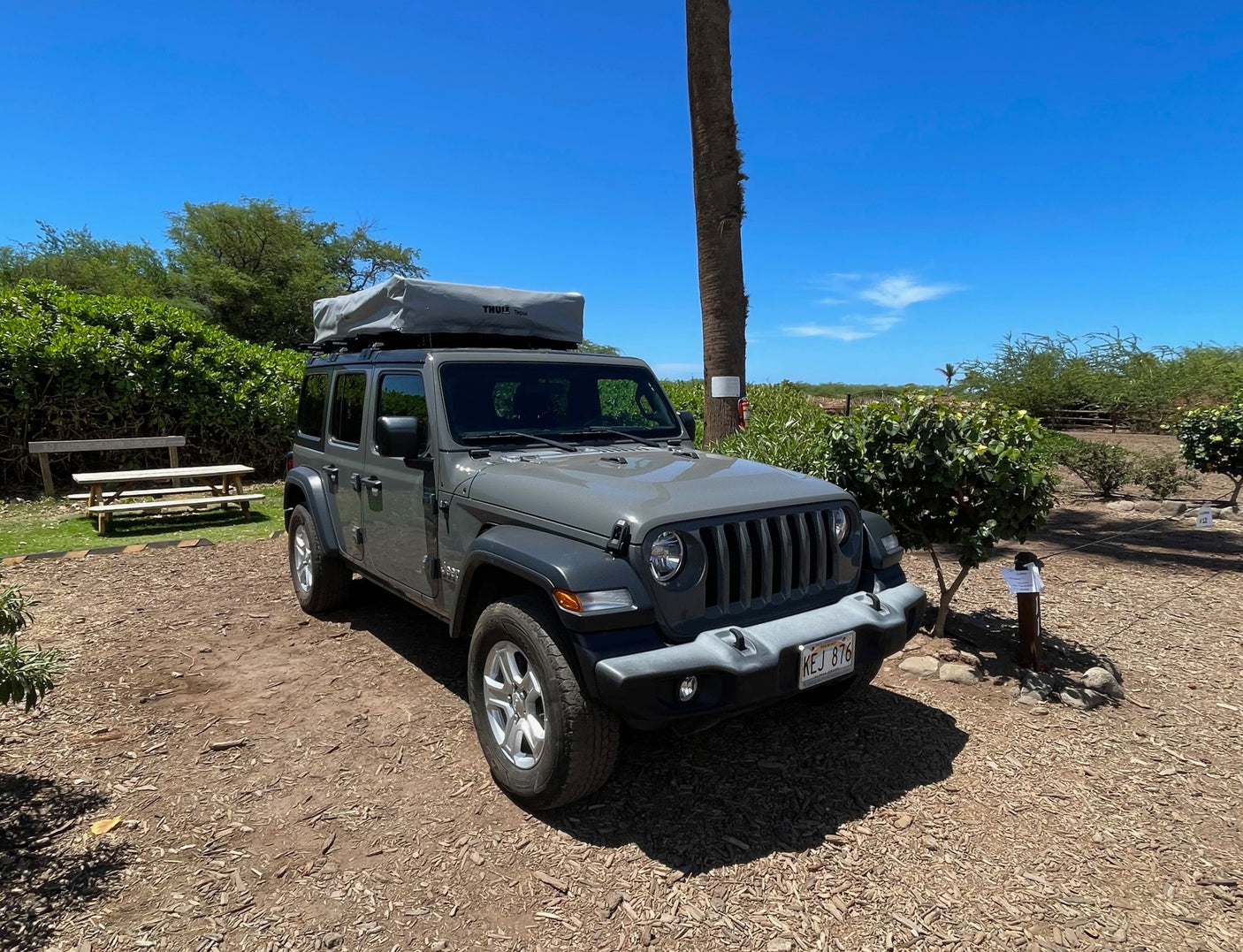 Grey Jeep Wrangler with rooftop tent, a unique rv rental for outdoor adventures under a clear blue sky.