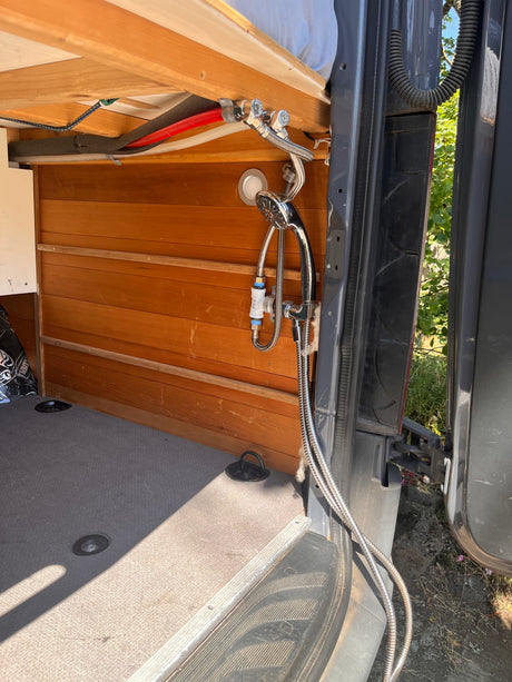 RV rental: Camper van's compact shower system, featuring a chrome faucet, flexible hoses, and wooden interior paneling.