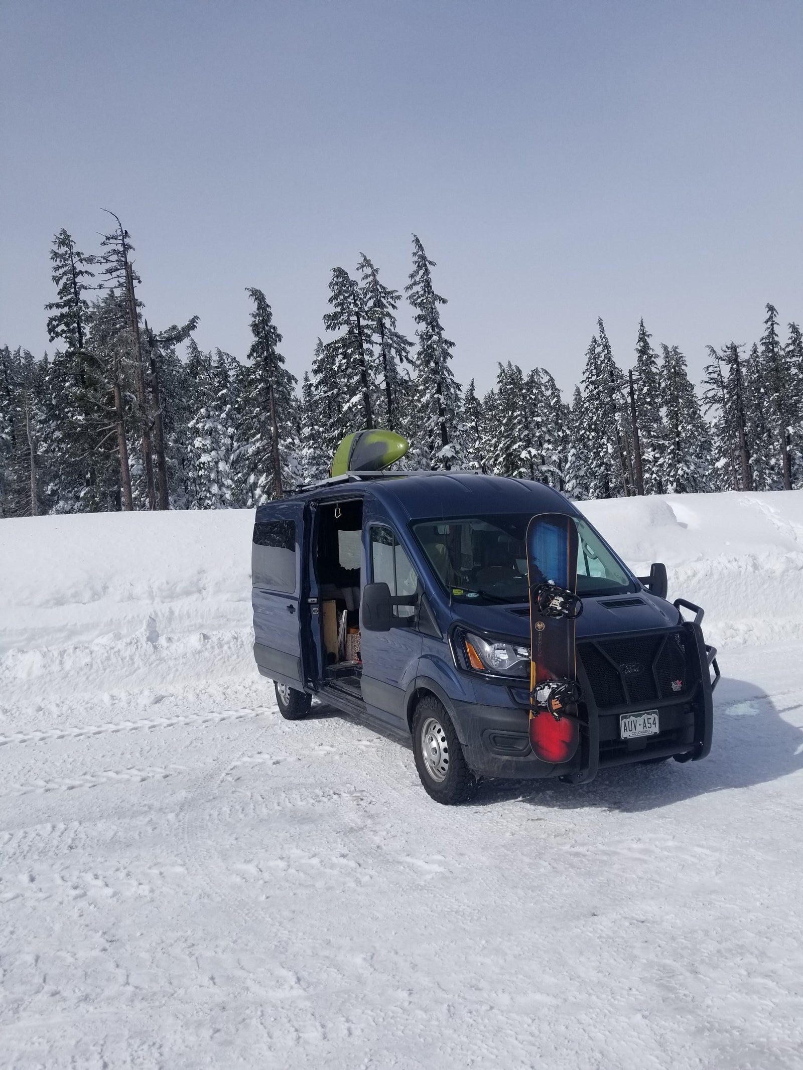 Blue van with snowboard & kayak, ideal for winter rv rental adventures in snowy forests.
