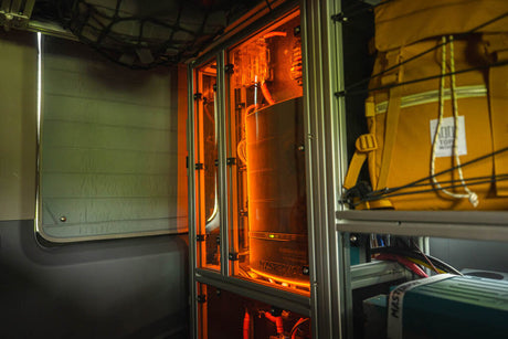 An RV rental's interior: orange-lit Mastervolt power system, insulated window, and backpack storage. Essential for off-grid adventures.