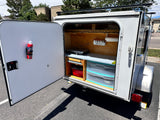 This RV rental teardrop camper showcases its organized outdoor kitchen with stove, spice rack, and storage.