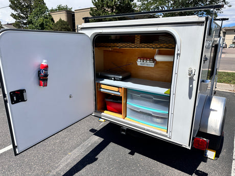 This RV rental teardrop camper showcases its organized outdoor kitchen with stove, spice rack, and storage.