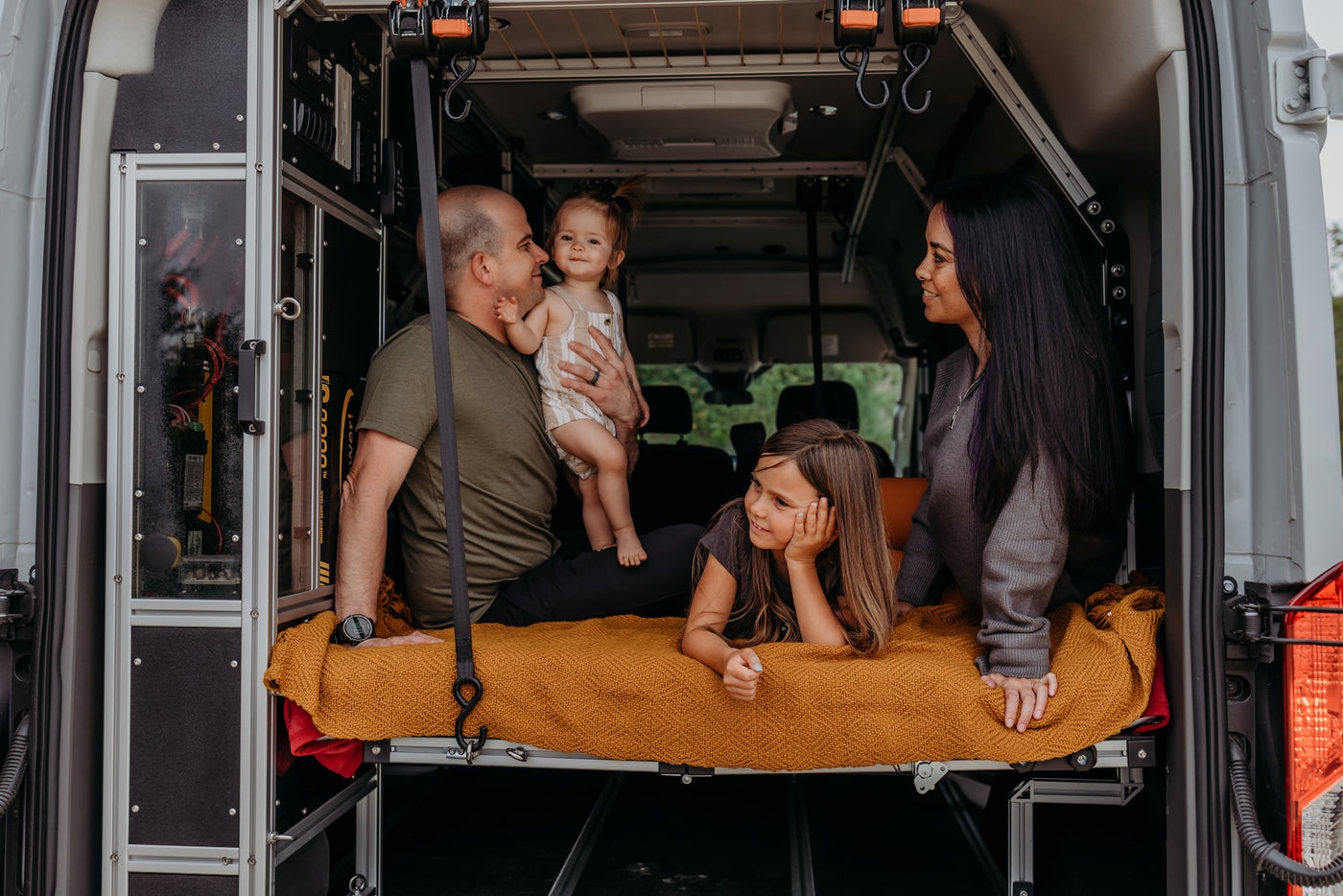 A family of four (parents, two daughters) enjoys a cozy moment in their rv rental camper van on a yellow blanket. — photo 12
