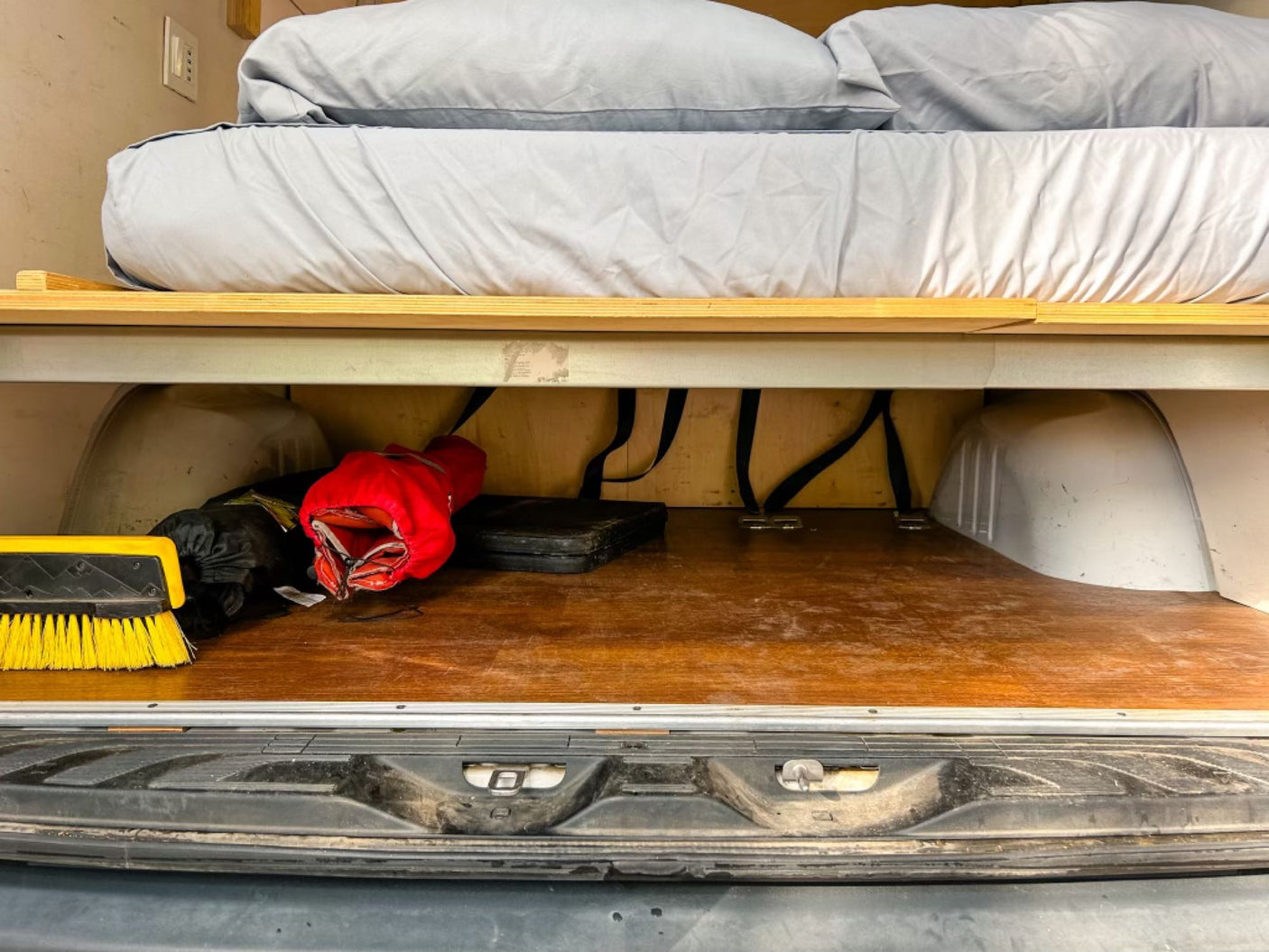 Compact RV rental interior: elevated bed with spacious under-bed storage for gear like brushes & bags.