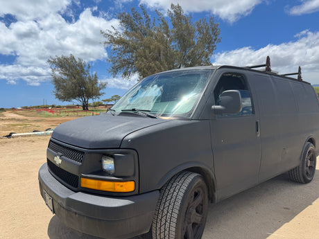 Matte black cargo van for rv rental, parked on a dirt lot under a sunny, cloudy sky. Ready for adventure.