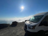 This white RV rental van enjoys a clear day above a cloud inversion from a dirt mountain road with bright sun.