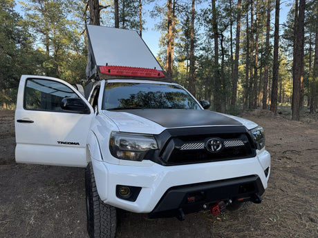 White Toyota Tacoma with open rooftop tent, red traction boards, & off-road gear. Great for an RV rental adventure!