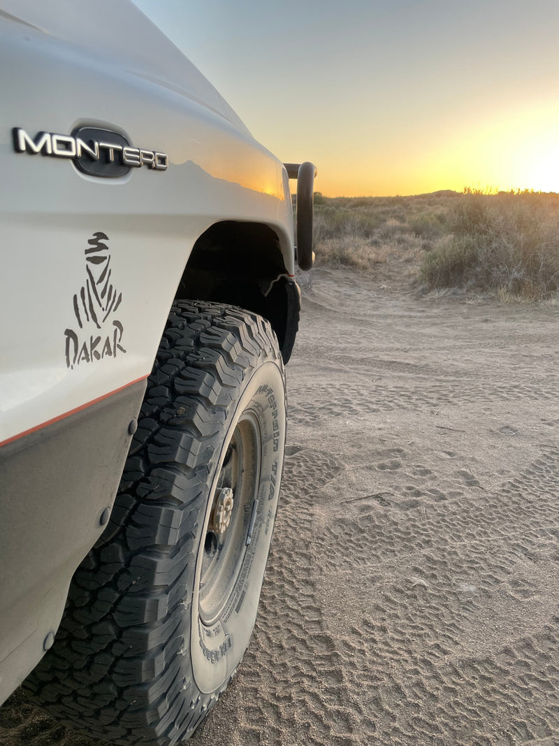 White Montero SUV with Dakar sticker & off-road tires on a sandy desert track at sunset. Your rugged rv rental adventure. — photo 4