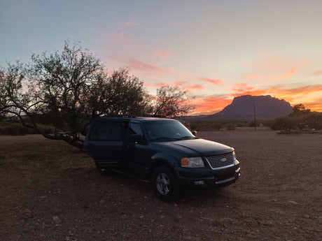 Dark SUV on a dirt road at sunset by mountains & trees, driver door open. An outdoor adventure, perfect for an rv rental getaway.