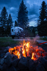 Cozy campfire at dusk with a truck camper nearby. Plan your next RV rental adventure in nature!