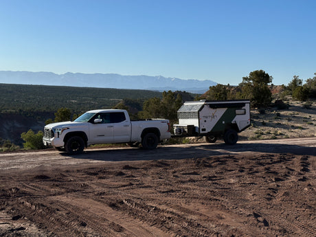 White pickup towing a TETON off-road RV rental on a dirt trail. Scenic desert mountains for your next adventure camping trip.