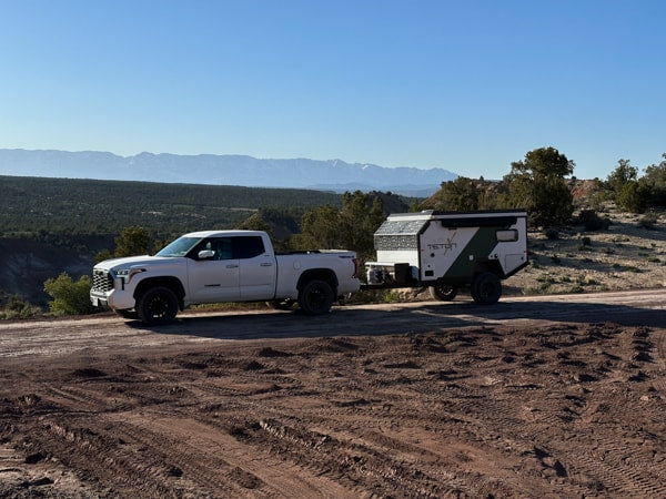 White pickup towing a TETON off-road RV rental on a dirt trail. Scenic desert mountains for your next adventure camping trip. — photo 11