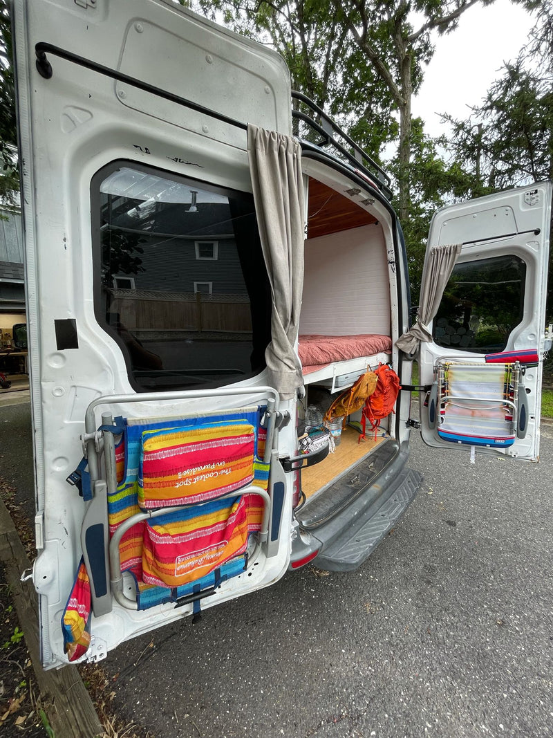 Open white camper van rear, revealing a bed, stored gear, and door-mounted beach chairs/drying rack. Great for an RV rental trip. — photo 15