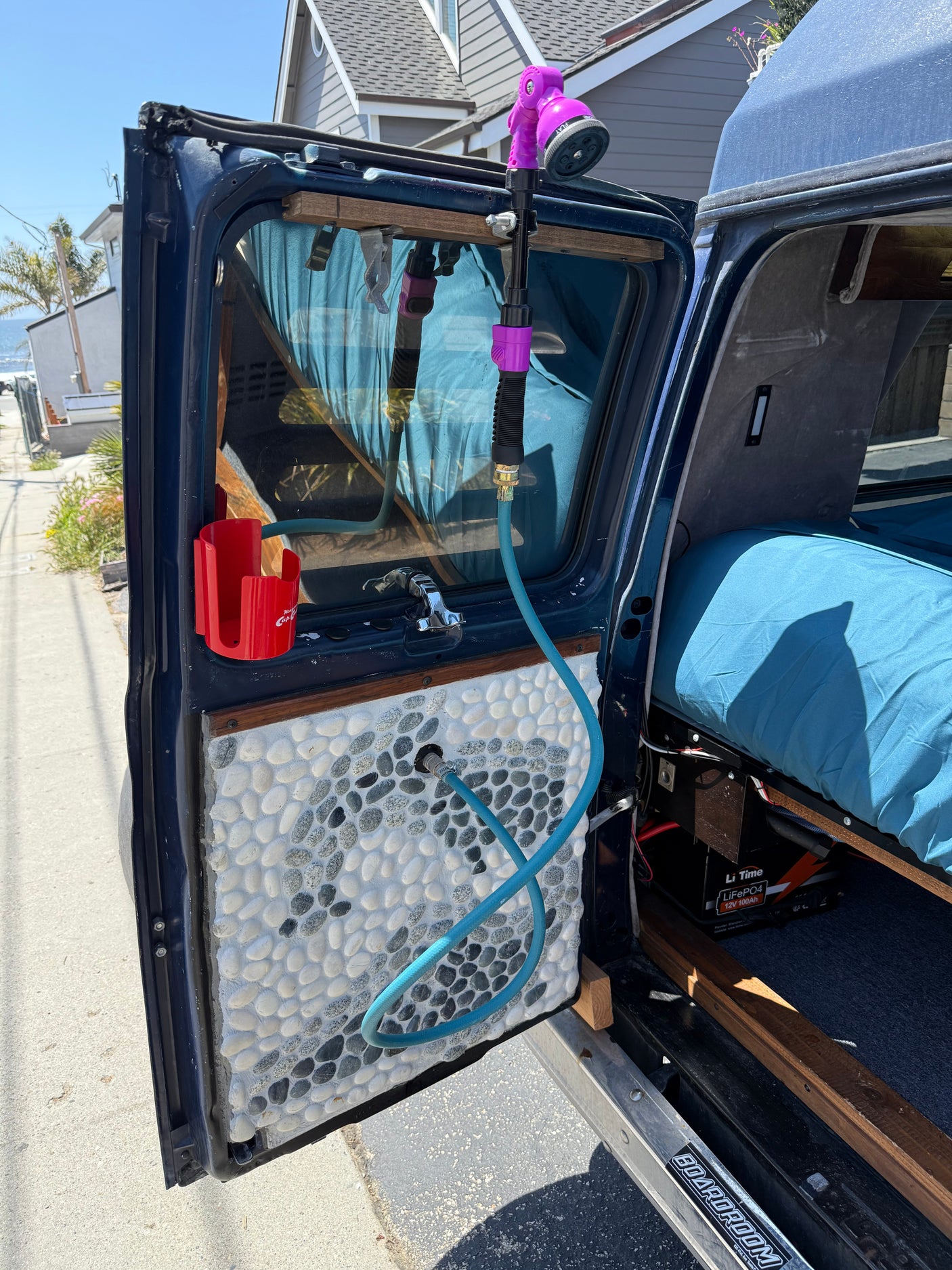 RV rental camper van with open door, showing a custom pebble panel, outdoor shower setup, and LiFePO4 battery.