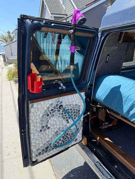 RV rental camper van with open door, showing a custom pebble panel, outdoor shower setup, and LiFePO4 battery.